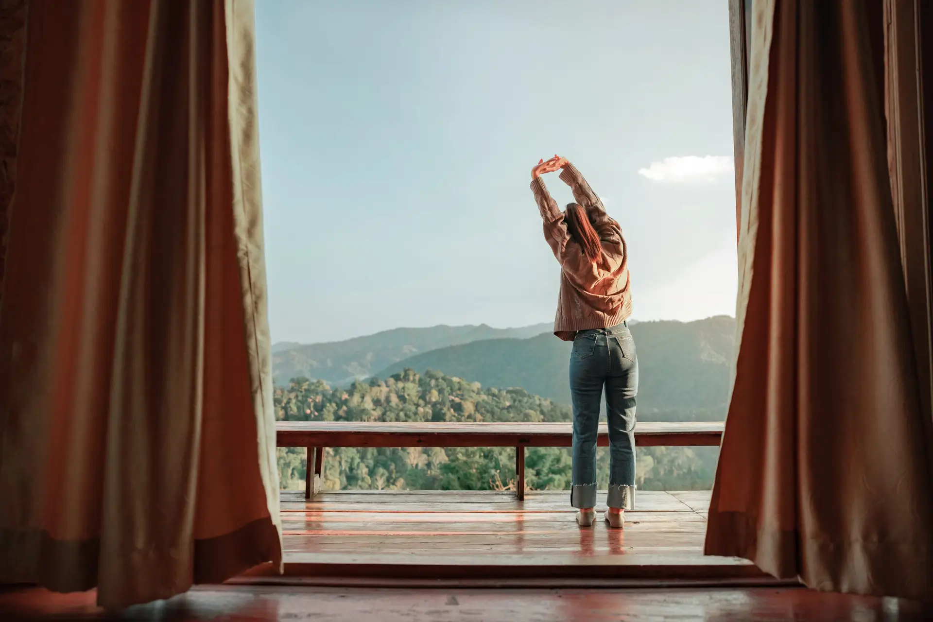 A woman stretching on a balcony overlooking a scenic mountain view, embracing the morning light.