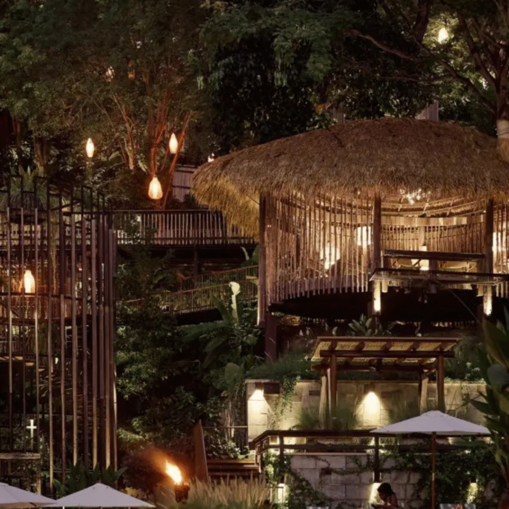 Thatched-roof bamboo lounge area lit up at night in the jungle