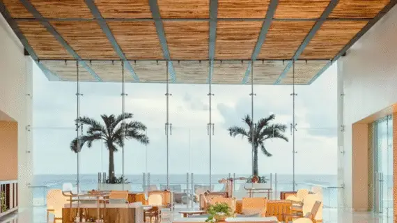 Indoor lounge and dining space with panoramic sea views, natural textures, and contemporary Mexican design.