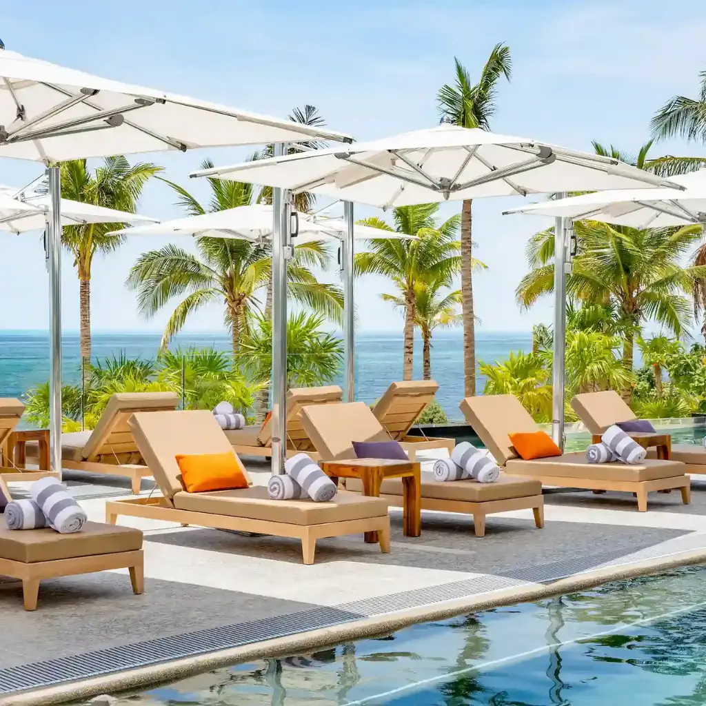 Panoramic view of the main pool at Hotel Mousai Cancun, surrounded by lounge chairs and ocean views.