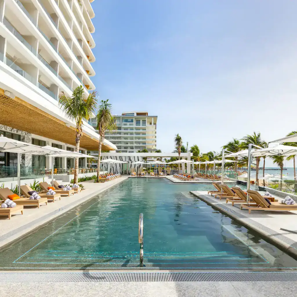 View of the main pool at Hotel Mousai Cancun, with lounge chairs and wooden tables